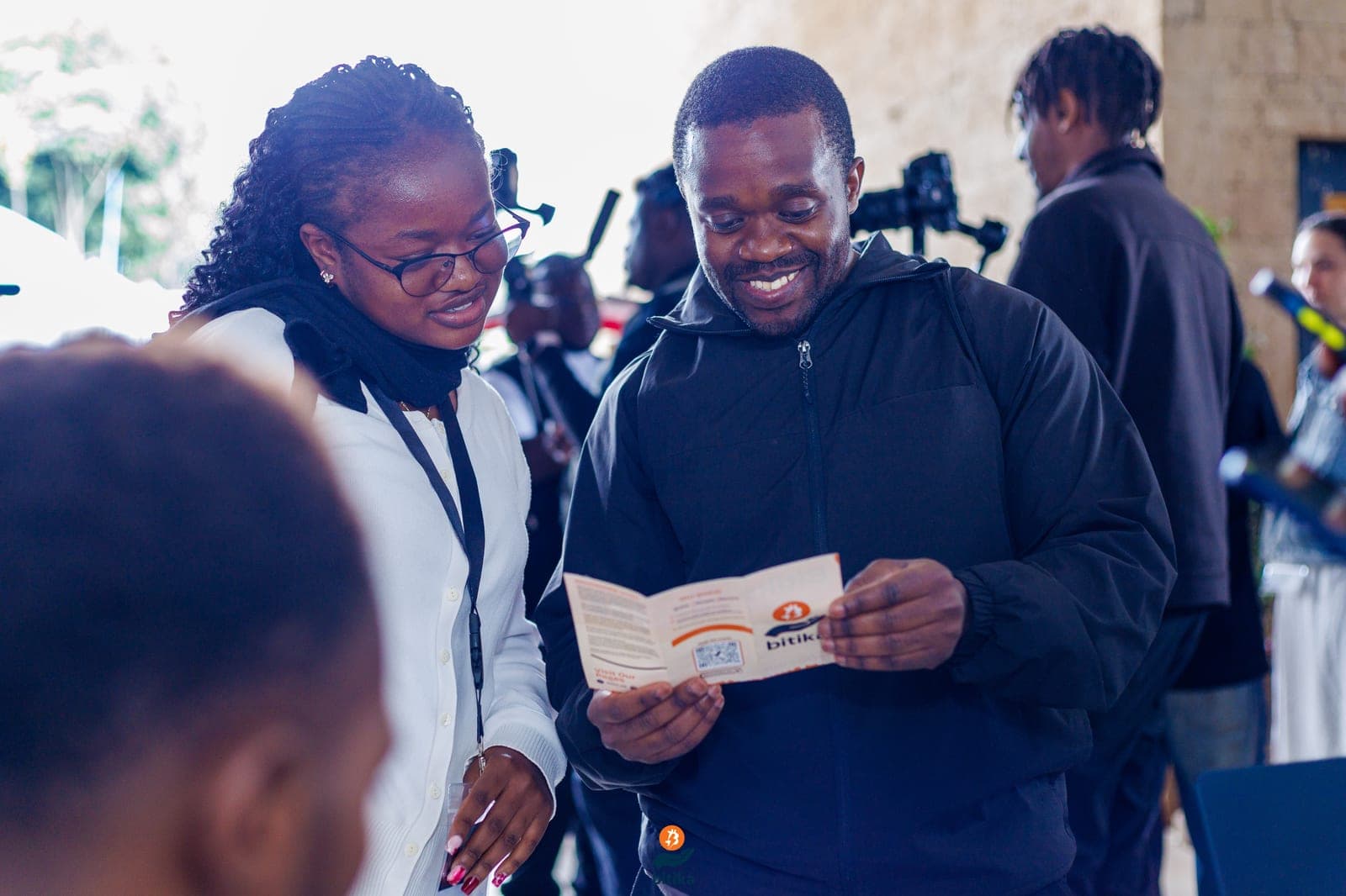 Two people smiling as they read a Bitika brochure together at an event