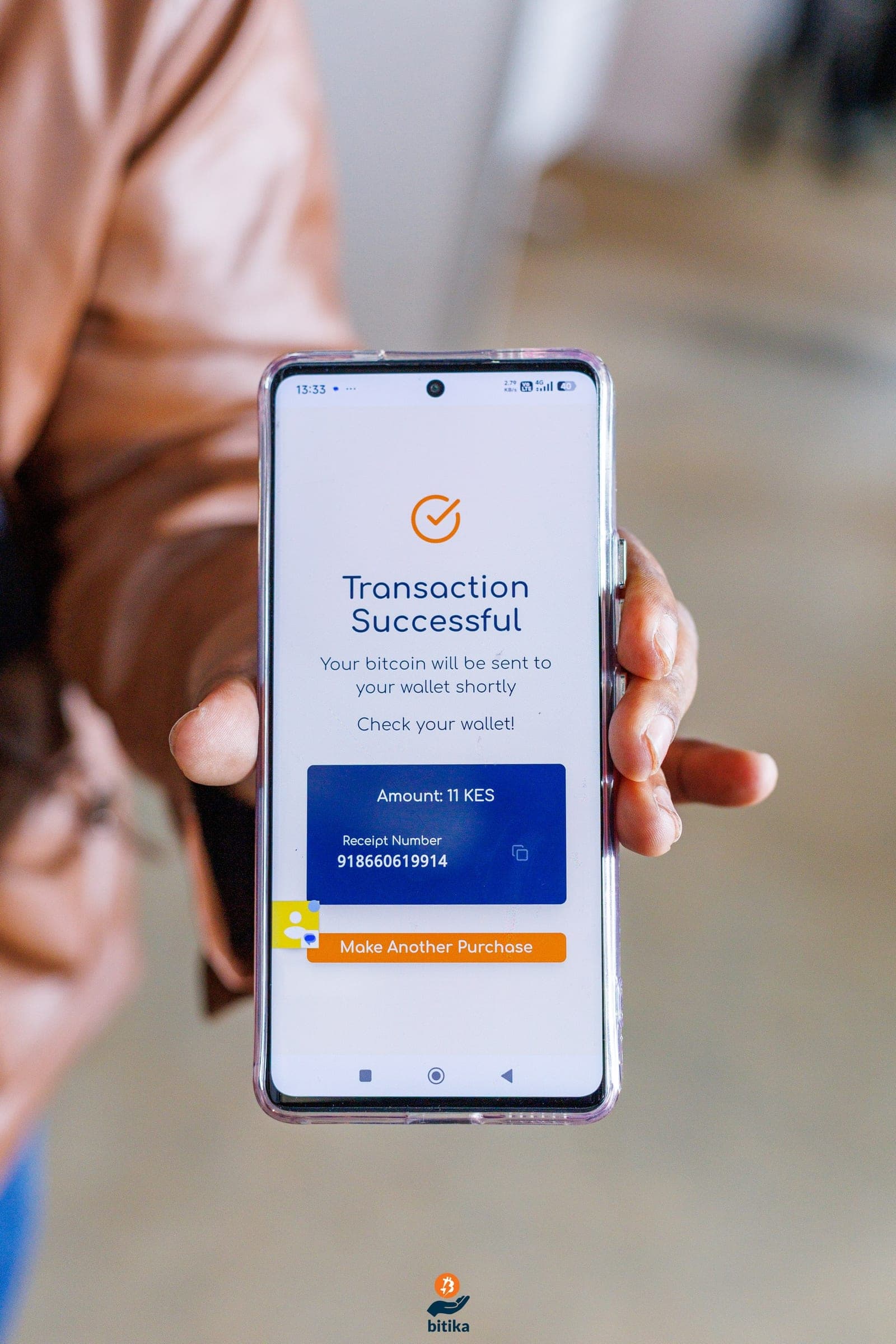A hand holding a phone showing the Bitika 'Transaction Successful' screen